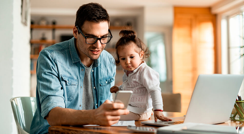 Father at home looking at his smart phone being watched by his young daughter